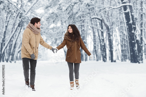 Couple Walking Holding Hands Talking In Winter Park, Full Length