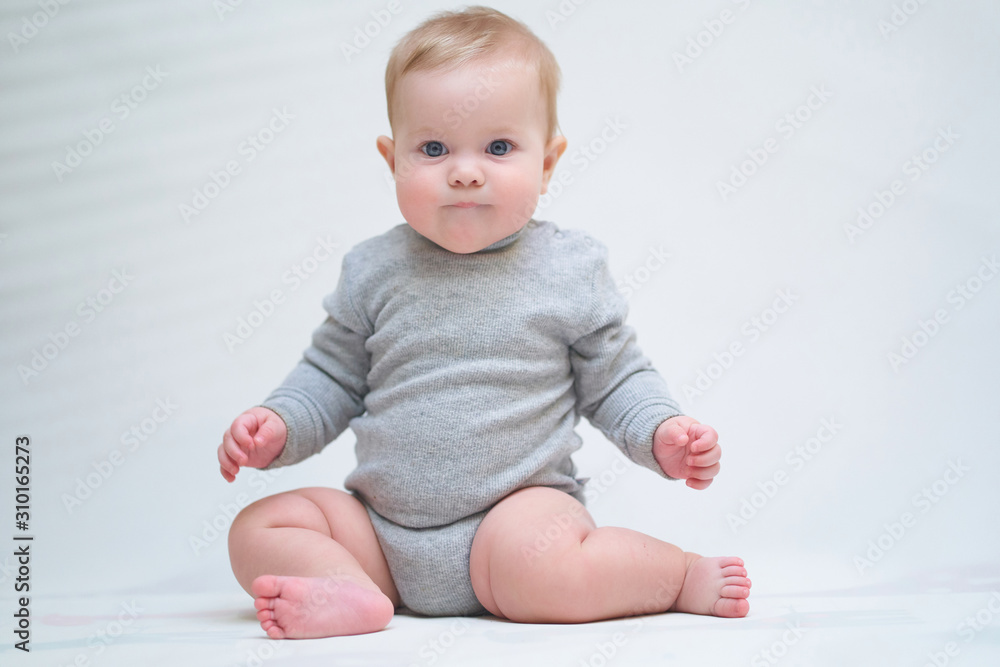 A 6 month old baby learns to sit down. photo on a neutral background A 6 month old baby learns to sit down. photo on a neutral background
