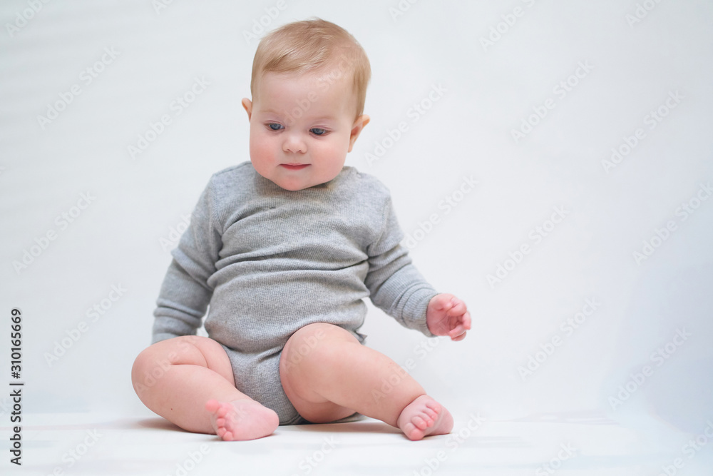 A 6 month old baby learns to sit down. photo on a neutral background A 6 month old baby learns to sit down. photo on a neutral background