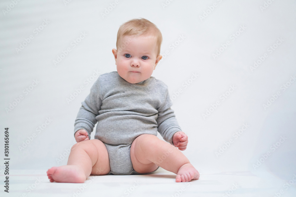 A 6 month old baby learns to sit down. photo on a neutral background A 6 month old baby learns to sit down. photo on a neutral background