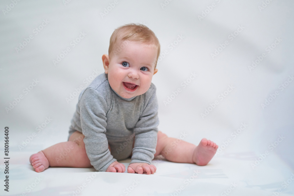 A 6 month old baby learns to sit down. photo on a neutral background A 6 month old baby learns to sit down. photo on a neutral background