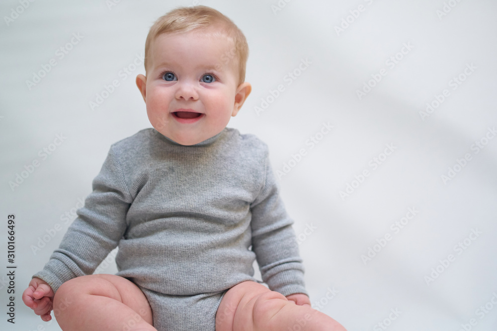 A 6 month old baby learns to sit down. photo on a neutral background A 6 month old baby learns to sit down. photo on a neutral background