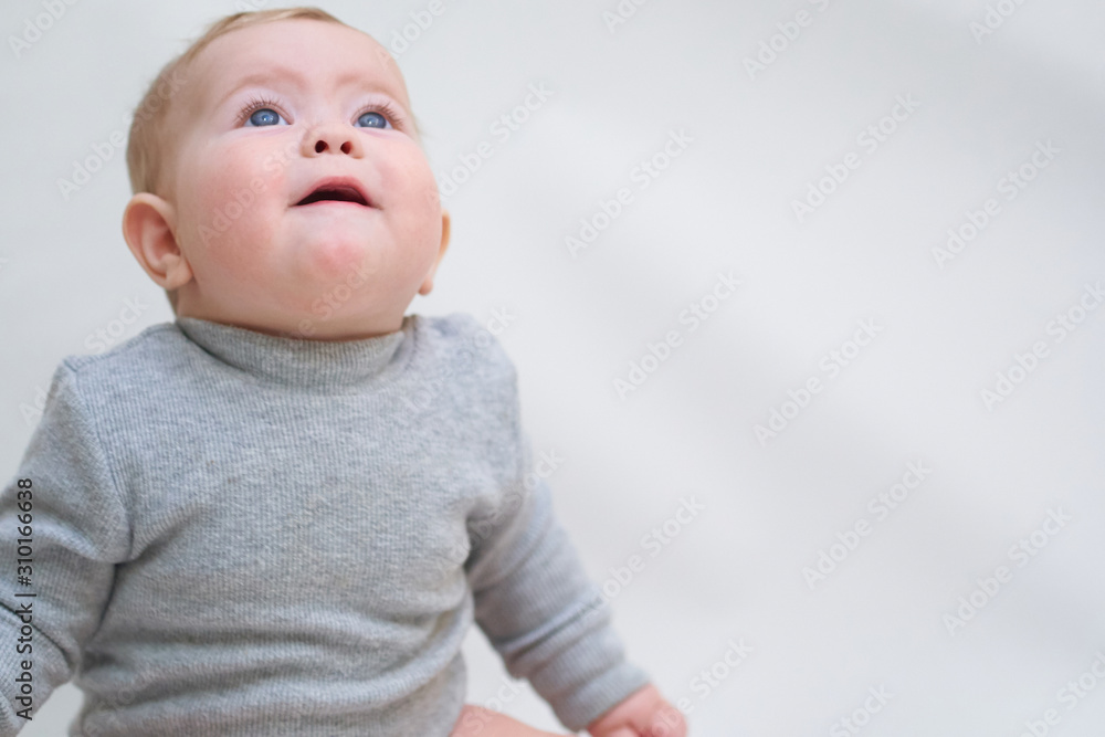 A 6 month old baby learns to sit down. photo on a neutral background A 6 month old baby learns to sit down. photo on a neutral background