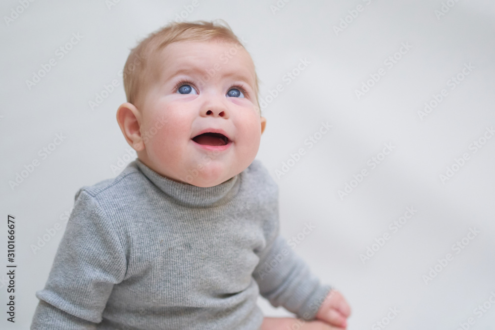 A 6 month old baby learns to sit down. photo on a neutral background A 6 month old baby learns to sit down. photo on a neutral background