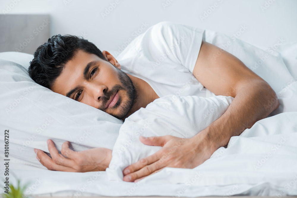 handsome bi-racial man lying in bed and looking at camera in morning handsome bi-racial man lying in bed and looking at camera in morning