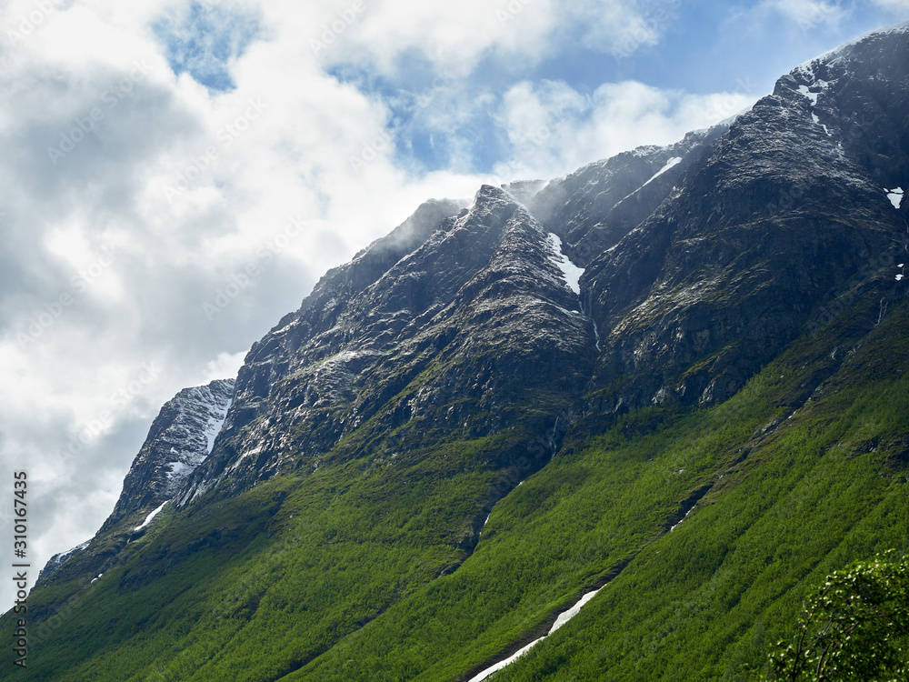 Closeup on snow covered fjords of Norway with ice and snow on the steep mountain edges. Clouds hanging low on the mountain peaks.