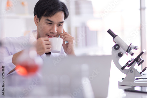 Asian scientists wearing white coats Sit in the lab and relax with a coffee.