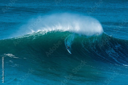 Tall wave of the Atlantic Ocean carrying the surfer towards the shore of Nazare, Portugal photo