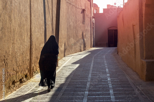 A woman in traditional black Islamic clothing walks the empty morning street of the eastern city. Back view. © Serhii