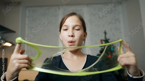 The girl on the background of the Christmas tree inflates slime. Stress relief. photo