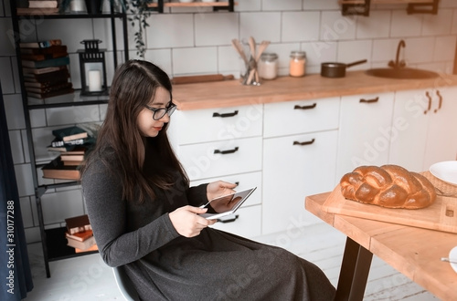 A young woman in the kitchen is looking at something on a tablet. Modern white kitchen.