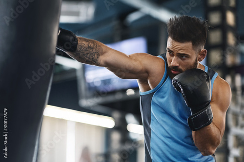 Sporty guy punching boxing bag at gym photo