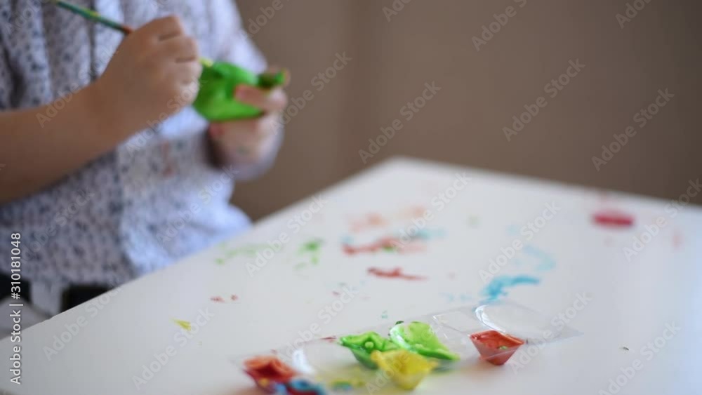 The hands of a litlle child with a brush paint an Easter egg in green color on the table. The hands of a litlle child with a brush paint an Easter egg in green color on the table.