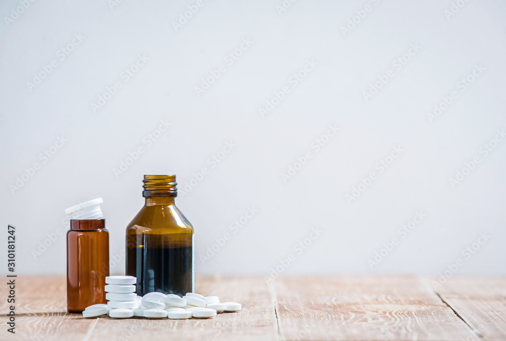Little medicine bottles and many white tablets on a wooden table. copy space