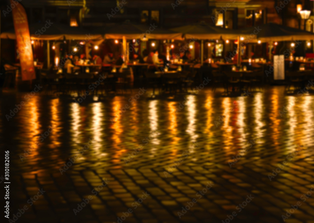 Blurred defocused street scene with restaurant, lights, reflection and people dining in the evening