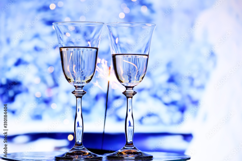 Two glasses with sparkling champagne wine and a garland with lights on the background of frosty patterns of branches in the snow. The winter mood of winter holidays. Two glasses with sparkling champagne wine and a garland with lights on the background of frosty patterns of branches in the snow. The winter mood of winter holidays.