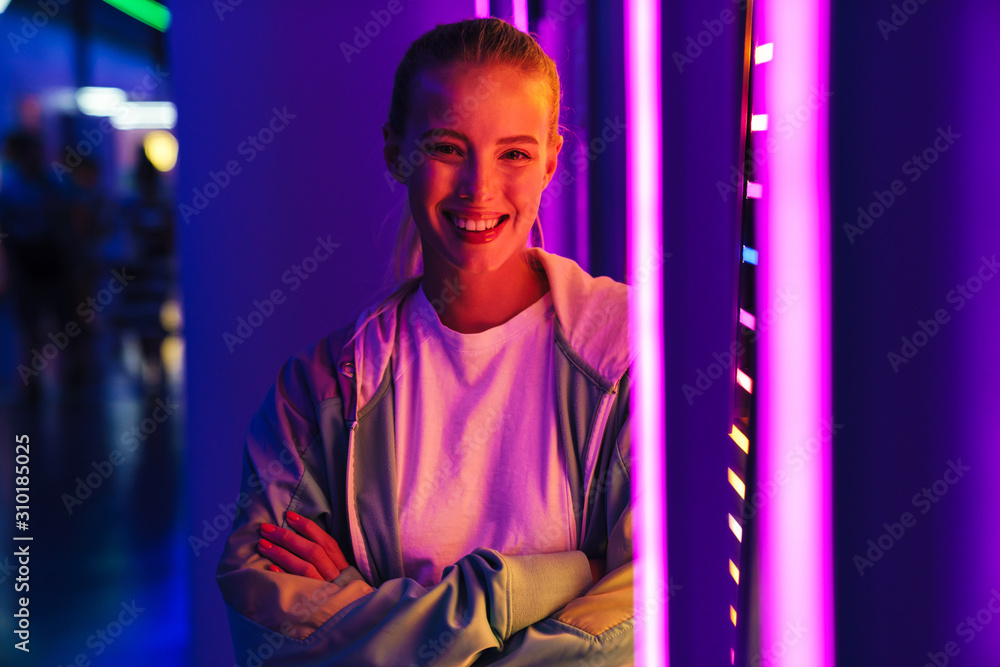 Image of young woman standing by multicolored neon illumination indoors Image of young woman standing by multicolored neon illumination indoors