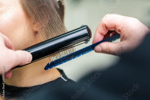 Hairdresser's hands straightening brown hair with hair irons, close up.