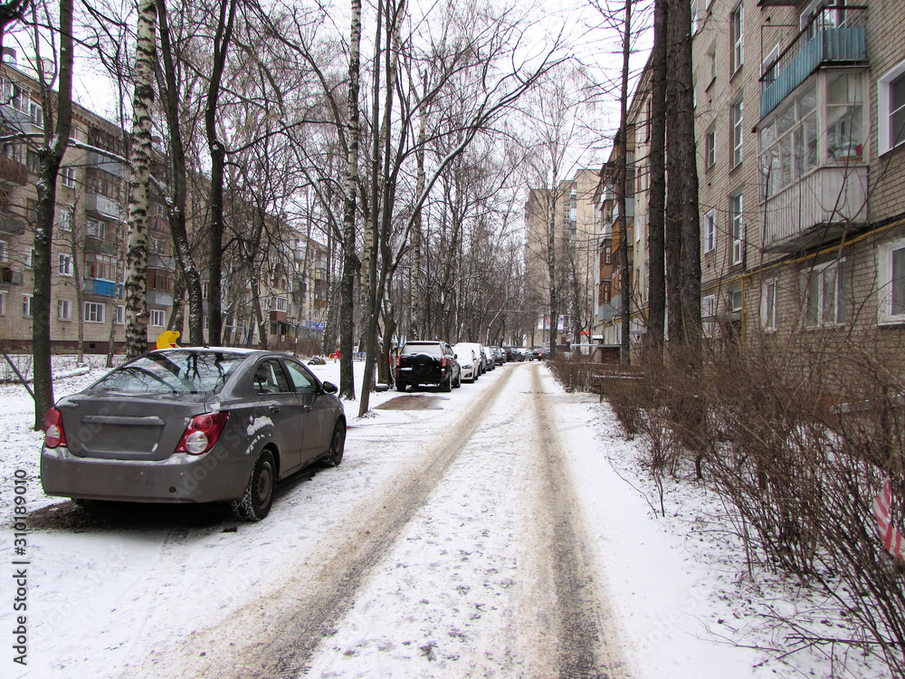 Winter road in the courtyard of an apartment building. Cars parked in the winter yard.