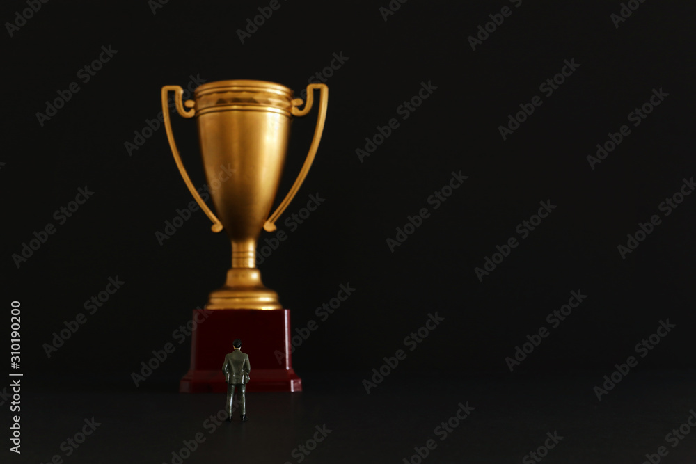 Concept image of business man stand in front of golden trophy. Idea of winning, achievement and success Concept image of business man stand in front of golden trophy. Idea of winning, achievement and success