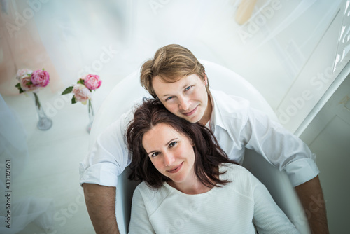 Positive charming young married couple woman brunette and blond sit in the bath and row paddle portraying a boat and the sea. Concept of a happy family life