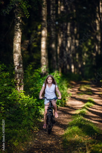 Little girl having fun on bike in the forest in autumn season