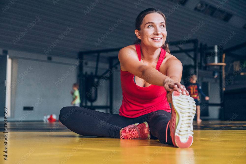 Naklejka premium Slim fit muscular brunette woman exercise in gym, lifting weights and doing pilates. Picture with dark evening mood and film color grading.