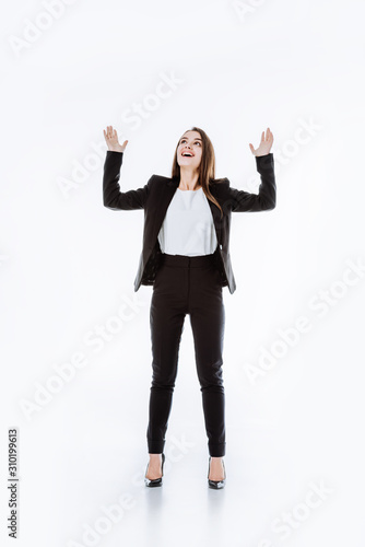happy businesswoman in suit with raised hands looking up isolated on white