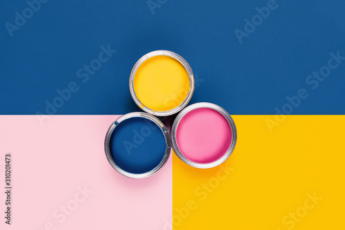 Renovation picture. Classic blue, yellow and pink background with three pain cans, central composition. Flat lay, top view, copy space.