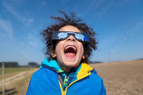 Junge blicht begeistert zur Sonnenfinsternis mit Schutzbrille