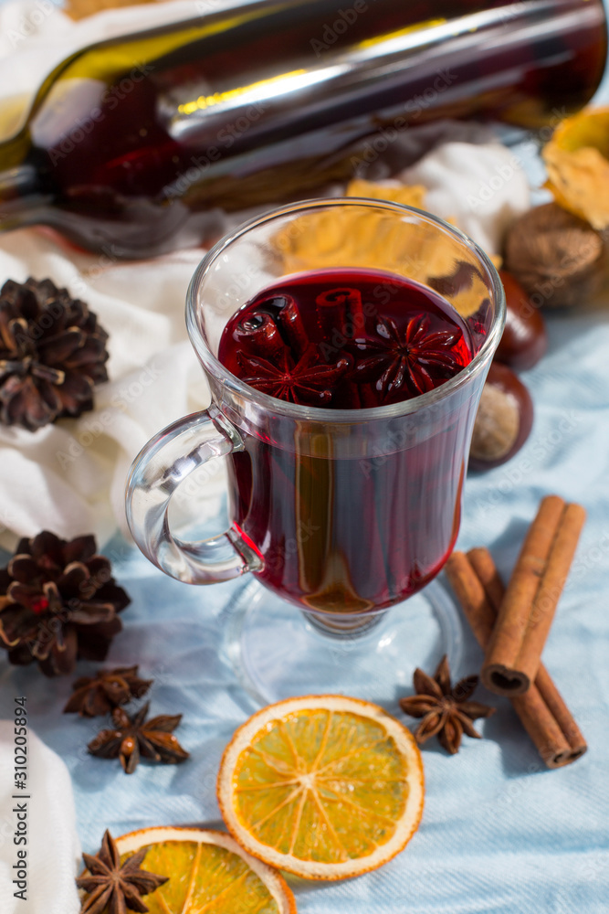 A cup of mulled wine with spices, bottle, dry leaves and oranges on table. Autumn mood, method to keep warm in the cold, copy space, morning light. A cup of mulled wine with spices, bottle, dry leaves and oranges on table. Autumn mood, method to keep warm in the cold, copy space, morning light.