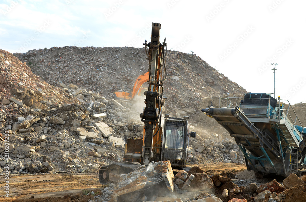 Fototapeta premium Salvaging and recycling building and construction materials. Excavator with hydraulic hammer work at landfill with concrete demolition waste. Reinforced concrete mobile shredder. Reuse concrete