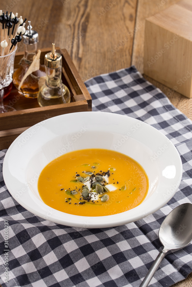 Pumpkin cream soup with seeds on fabric napkin on wooden table Pumpkin cream soup with seeds on fabric napkin on wooden table