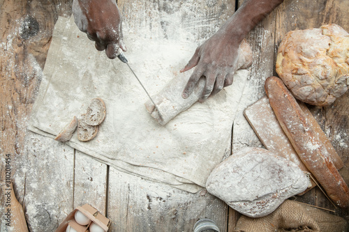 Top view of african-american man cooks fresh cereal, bread, bran on wooden table. Tasty eating, nutrition, craft product. Gluten-free food, healthy lifestyle, organic and safe manufacture. Handmade.