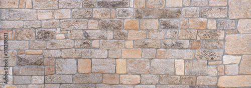 Panorama einer hellen, pastellfarbenen, alten, teils verwitterten Steinmauer aus unterschiedlichen Steinen photo