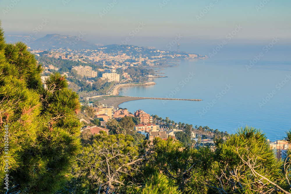 Panoramic view of the Spanish coast in Nerja from the Balcon de Europa. Sunny autumn day on the Mediterranean Sea with a view of a village and hills on the horizon. Blue sky with clouds and palm trees