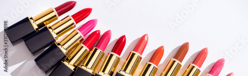 top view of assorted lipsticks in luxury tubes on white background, panoramic shot