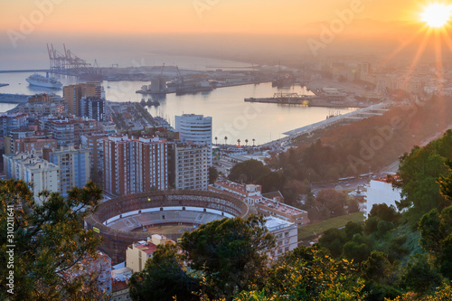 Deep sun on the horizon over Malaga. The city on the Spanish Costa del Sol at sunset with panoramic views of the harbor, houses, trees, bullring and blue sky over the mountains