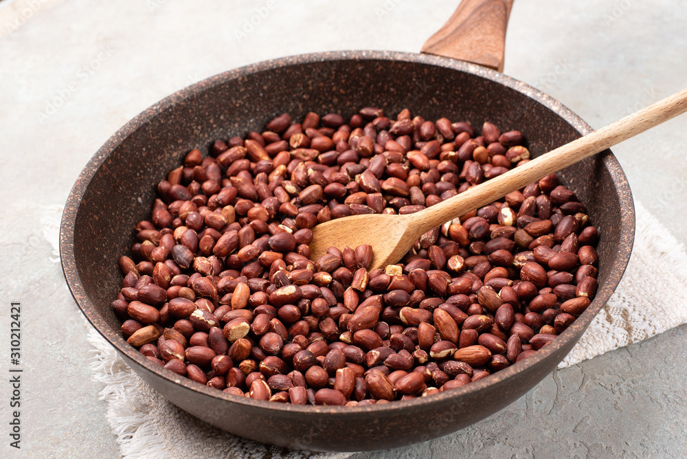 Fototapeta premium Roasted peanuts in a pan on a light gray textured background.