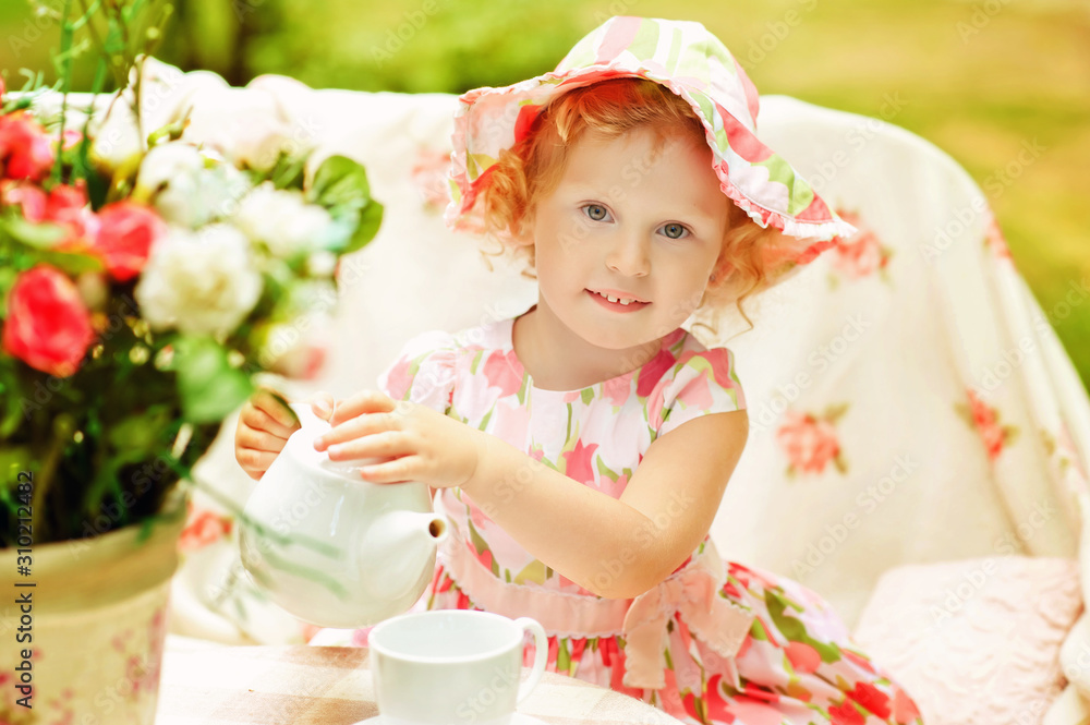 3 years old girl in pink dress and pink hat play outside. Young lady pours tea from teapot to cup. Summertime. Piquenique outdoors. Children game in adult life. Time for tea. Lifestyle near to nature 3 years old girl in pink dress and pink hat play outside. Young lady pours tea from teapot to cup. Summertime. Piquenique outdoors. Children game in adult life. Time for tea. Lifestyle near to nature