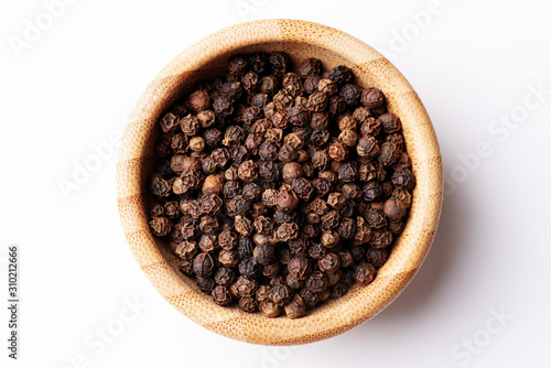 Whole black pepper in a small wooden bowl on a white background. Macro, flat lay.