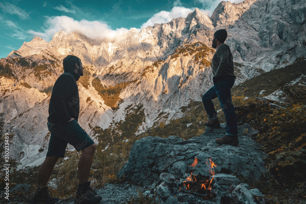 Obraz premium Two hikers in front of an impressive alpine mountain range at sunset.