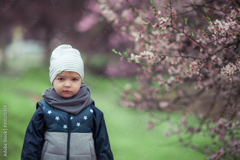 Child outdoors in autumn jacket and cap on the background of a garden with trees. Child outdoors in autumn jacket and cap on the background of a garden with trees.