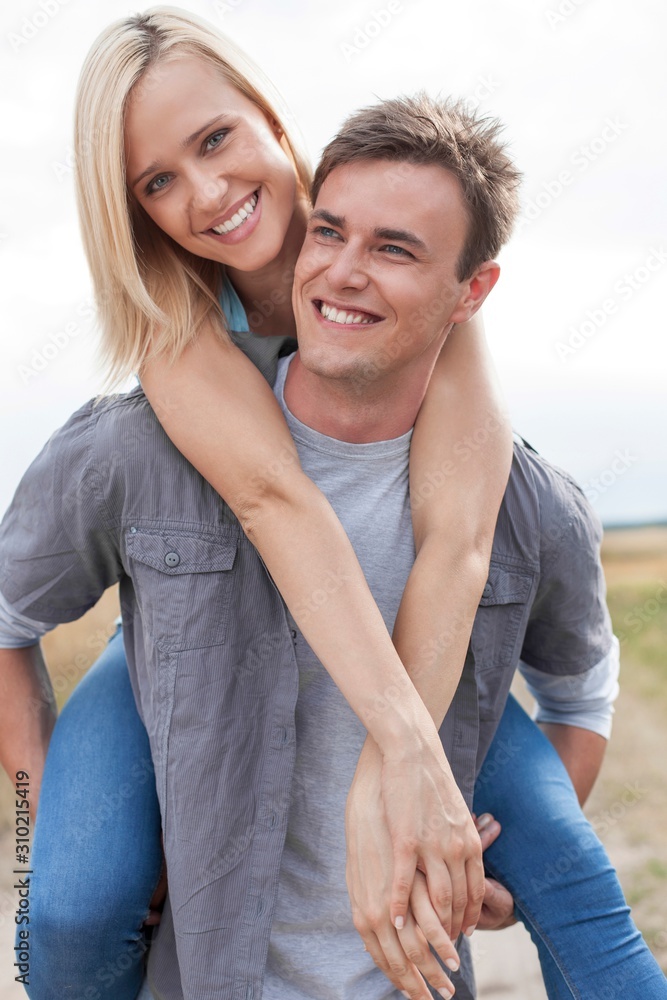 Fototapeta premium Happy young man giving piggyback ride to girlfriend on field