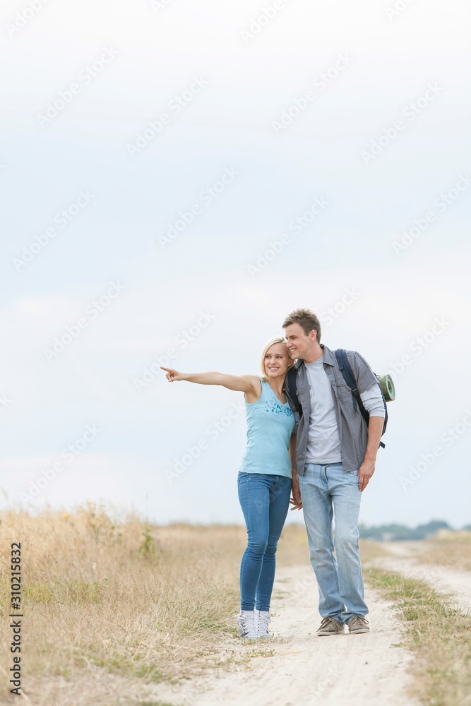 Young woman showing something to man while standing on trail at field Young woman showing something to man while standing on trail at field