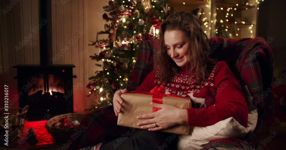 Happy emotional girl with a gift in her hands near the Christmas tree in decorated beautiful a cozy country house. Holiday christmas spirit Happy emotional girl with a gift in her hands near the Christmas tree in decorated beautiful a cozy country house. Holiday christmas spirit