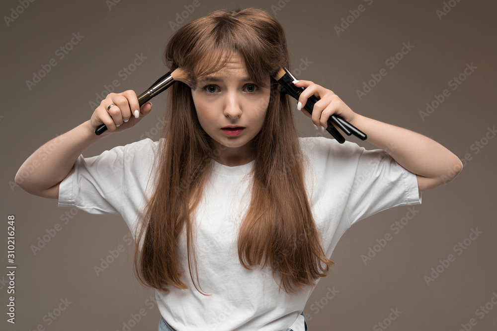 Obraz premium nice girl holds makeup brushes on her cheeks on a dark brown background