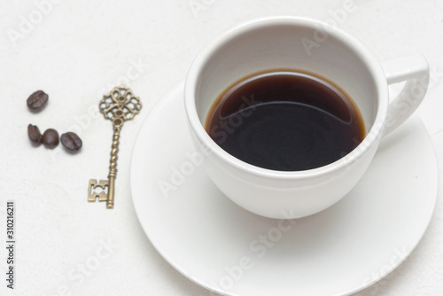 White tea cup with black coffee and golden key on white background.