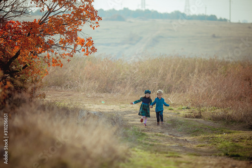 Boy and girl brother and sister running on the steppe road on the background of high yellow grass.