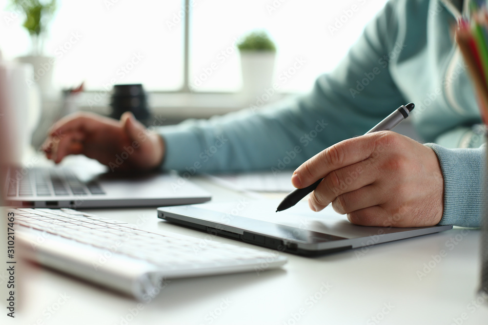 A young designer holds a pen from a tablet in his A young designer holds a pen from a tablet in his
